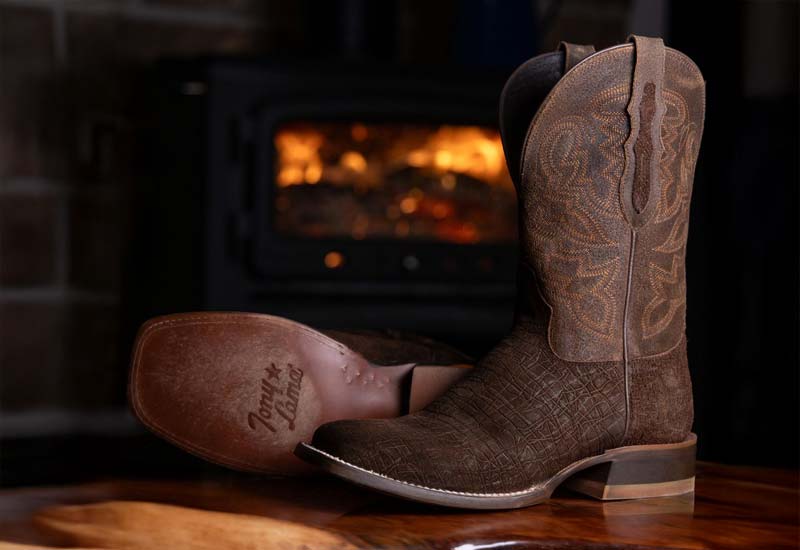 A pair of the Tucson 11” Western boot in Brown on a table in front of a fireplace.